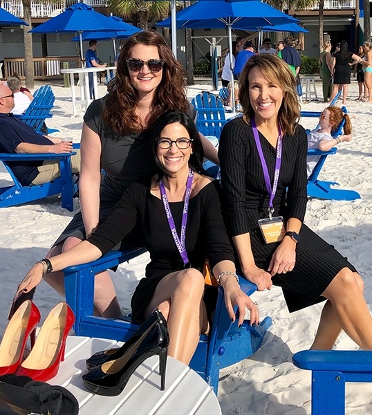 Three Mesa sleep apnea team members in black dresses sitting in wooden chairs on beach