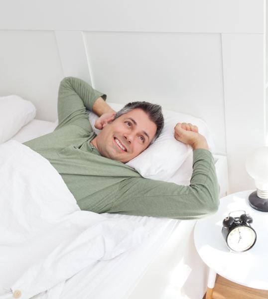 Man in green shirt stretching and smiling while laying in bed