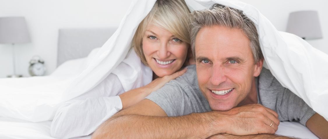 Older man and woman laying in bed on their stomachs and smiling after sleep apnea services in Mesa