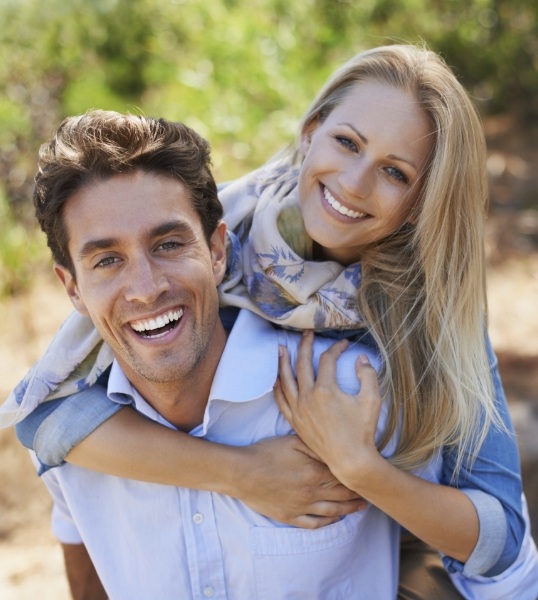 Smiling woman hugging smiling man from behind outdoors