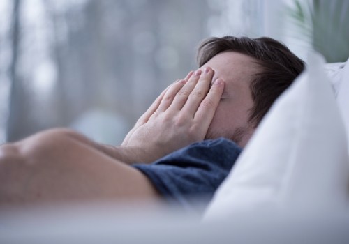 Man laying in bed and covering his face with his hands