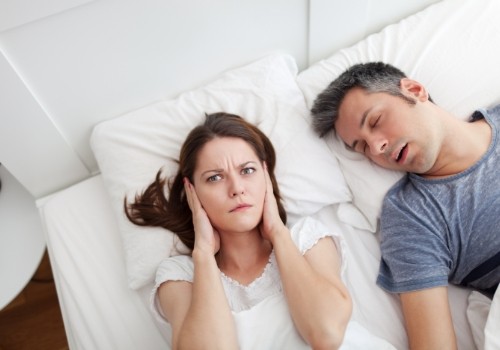Woman in bed covering her ears while man snores next to her