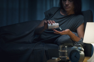 Woman in bed pouring sleeping pills into her hand